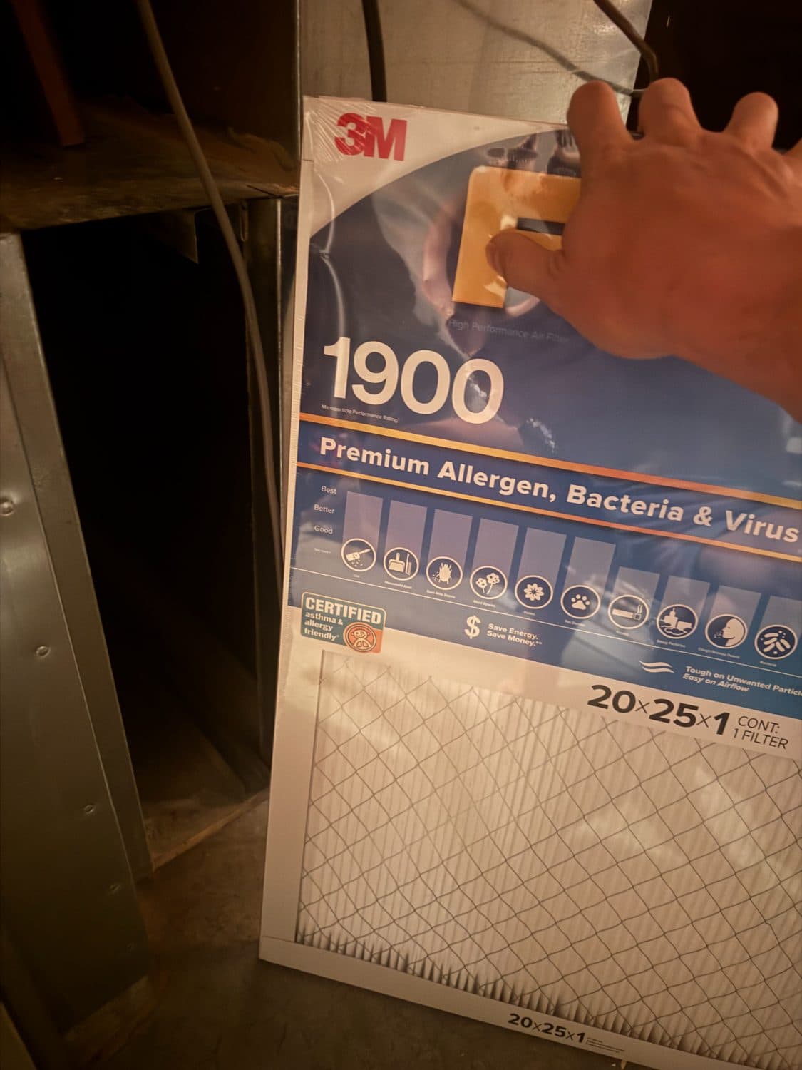 Hand holding a 20x25x1 allergen furnace filter next to a furnace