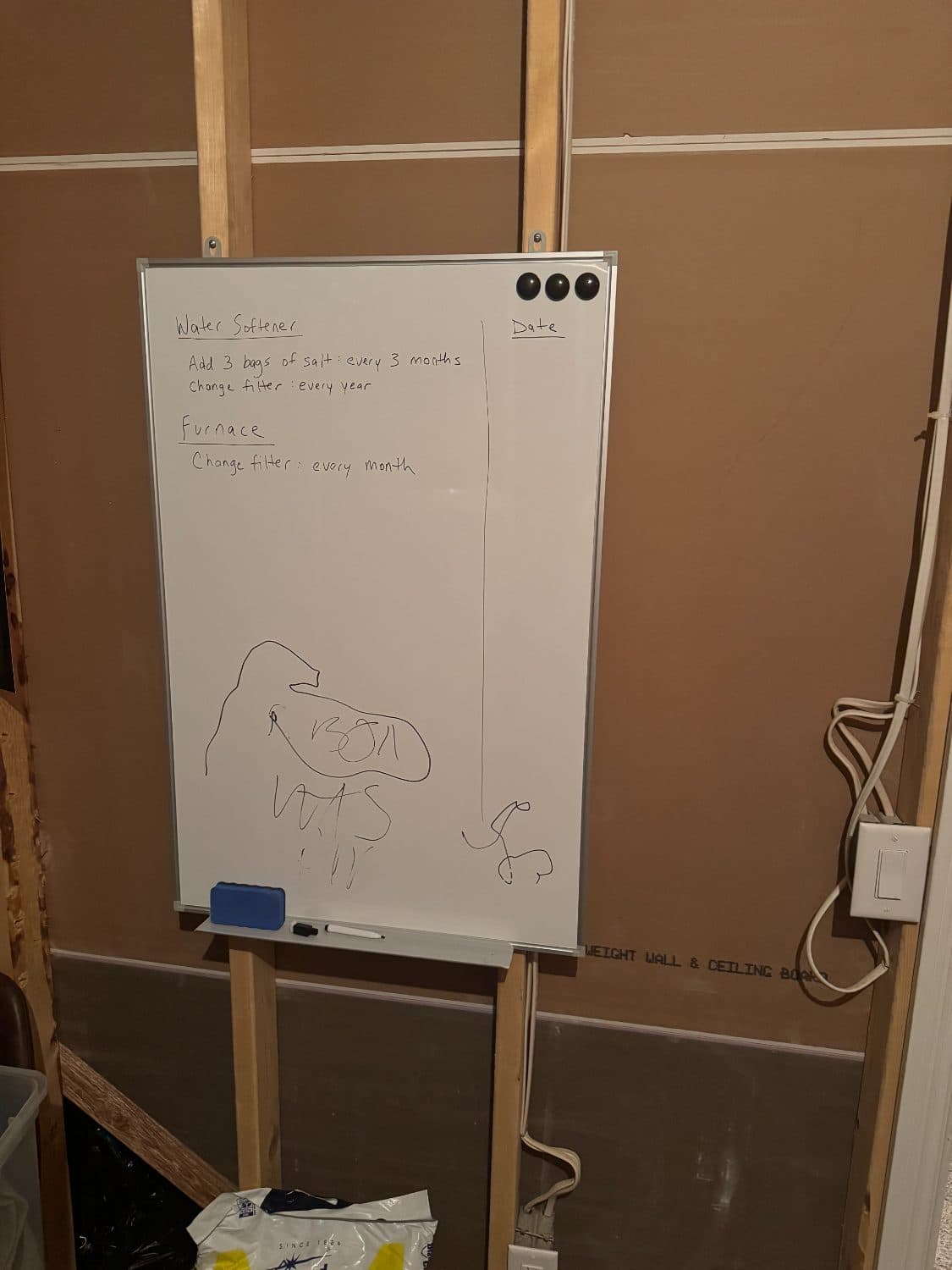 Whiteboard in a utility room listing water softener and furnace filter tasks, with an empty date column