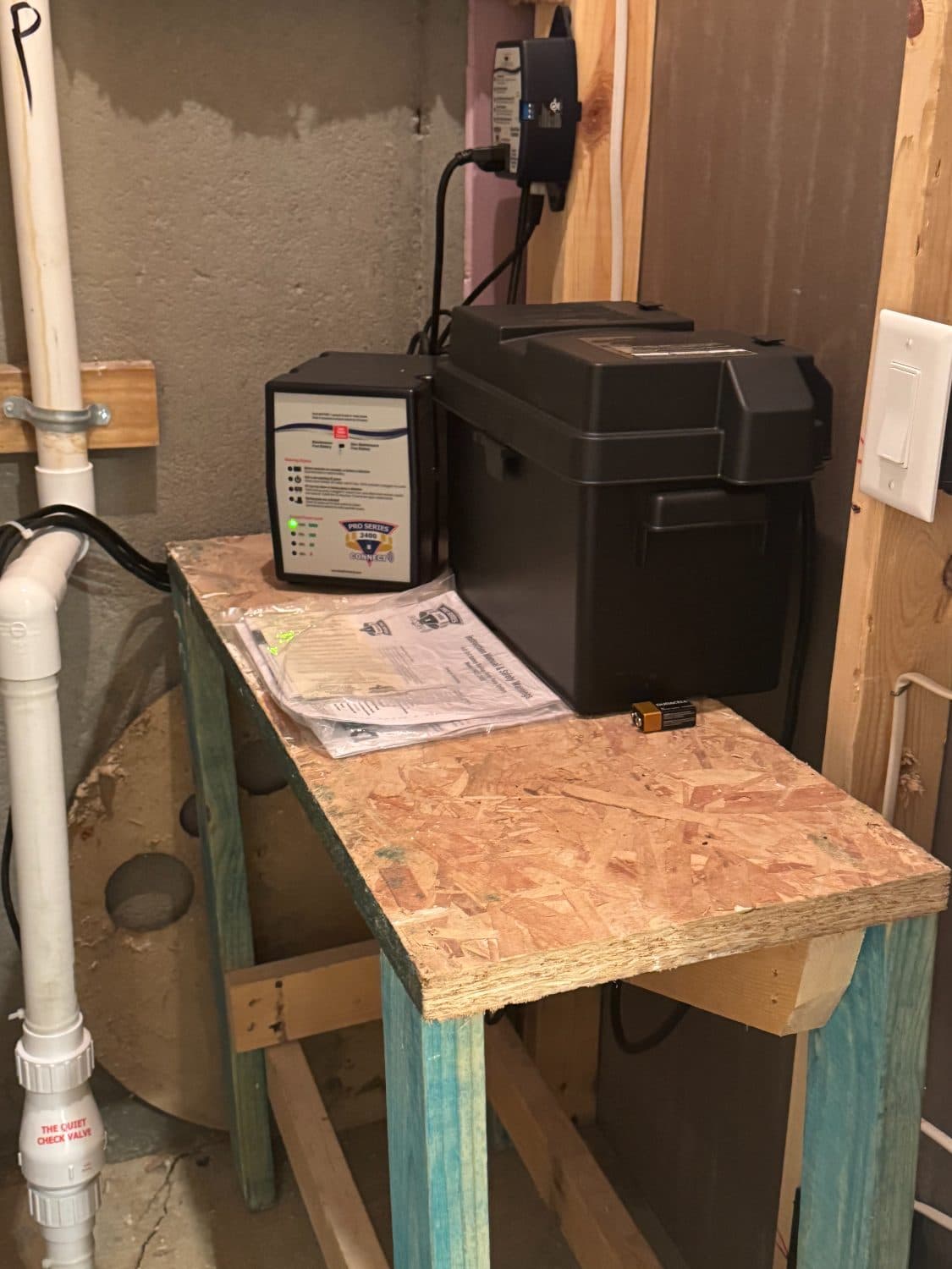 Sump pump backup battery controller and battery box on a wooden stand in an unfinished basement