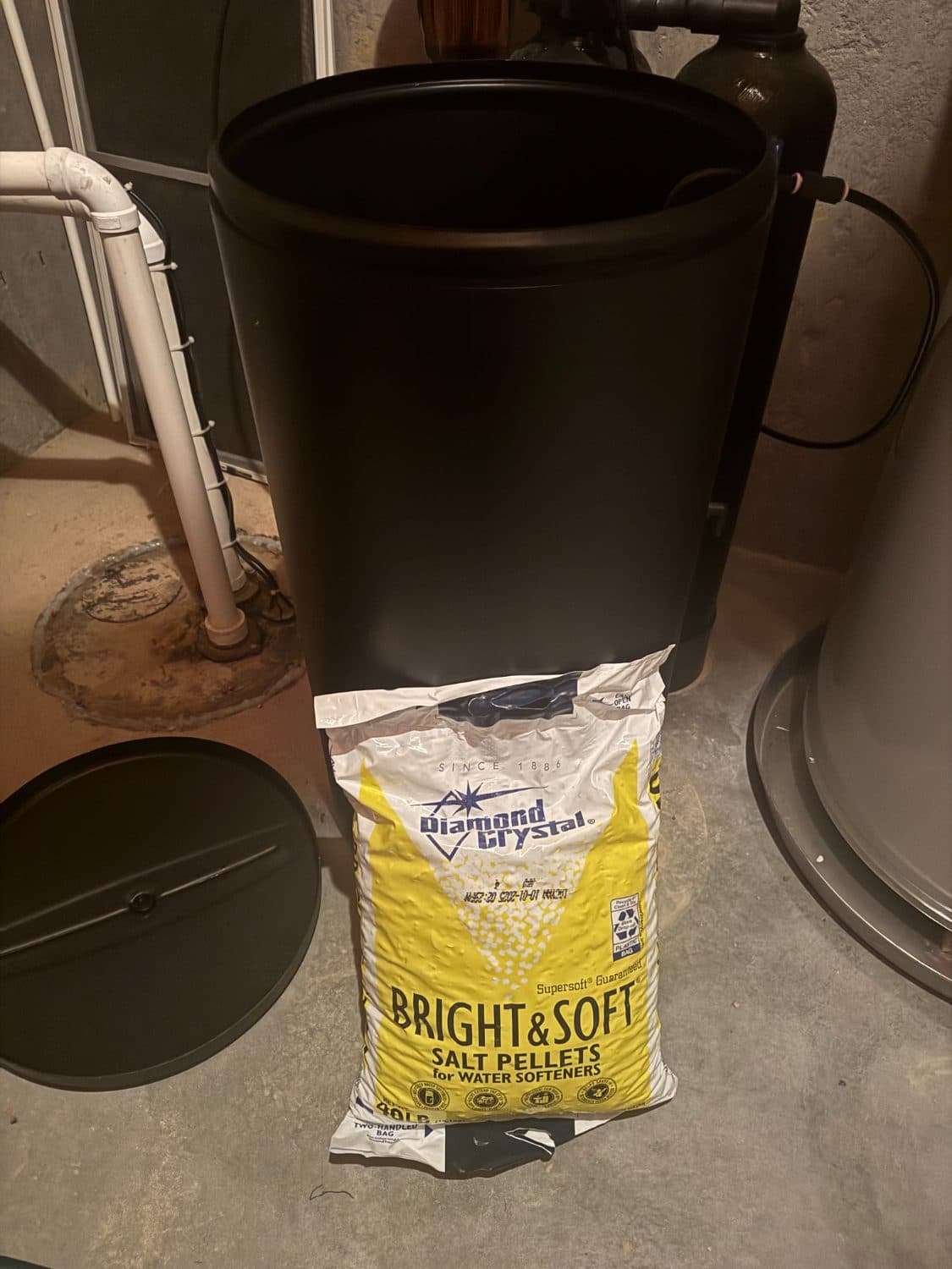 Forty pound bag of water softener salt pellets leaning against an open brine tank